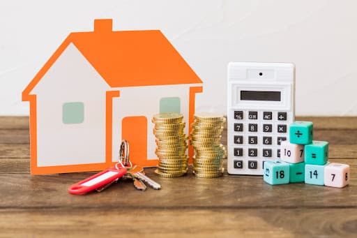 House, key, coins, calculator and math blocks on wooden table