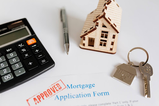 mortgage application form next to a calculator, pen, key and miniature house.